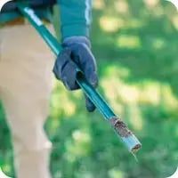 A Mainely Grass technician holding a soil core sample, assessing lawn health for optimal treatment.