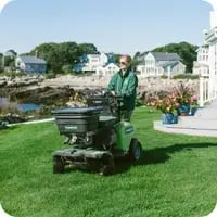 A Mainely Grass lawn care technician operating professional equipment with a branded service van in the background, delivering expert lawn care services.