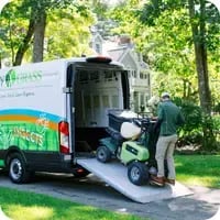 A Mainely Grass technician loading professional lawn care equipment into a branded service van, delivering expert lawn care services.