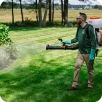 A Mainely Grass technician applying lawn pest control treatment for ticks to a healthy green lawn.